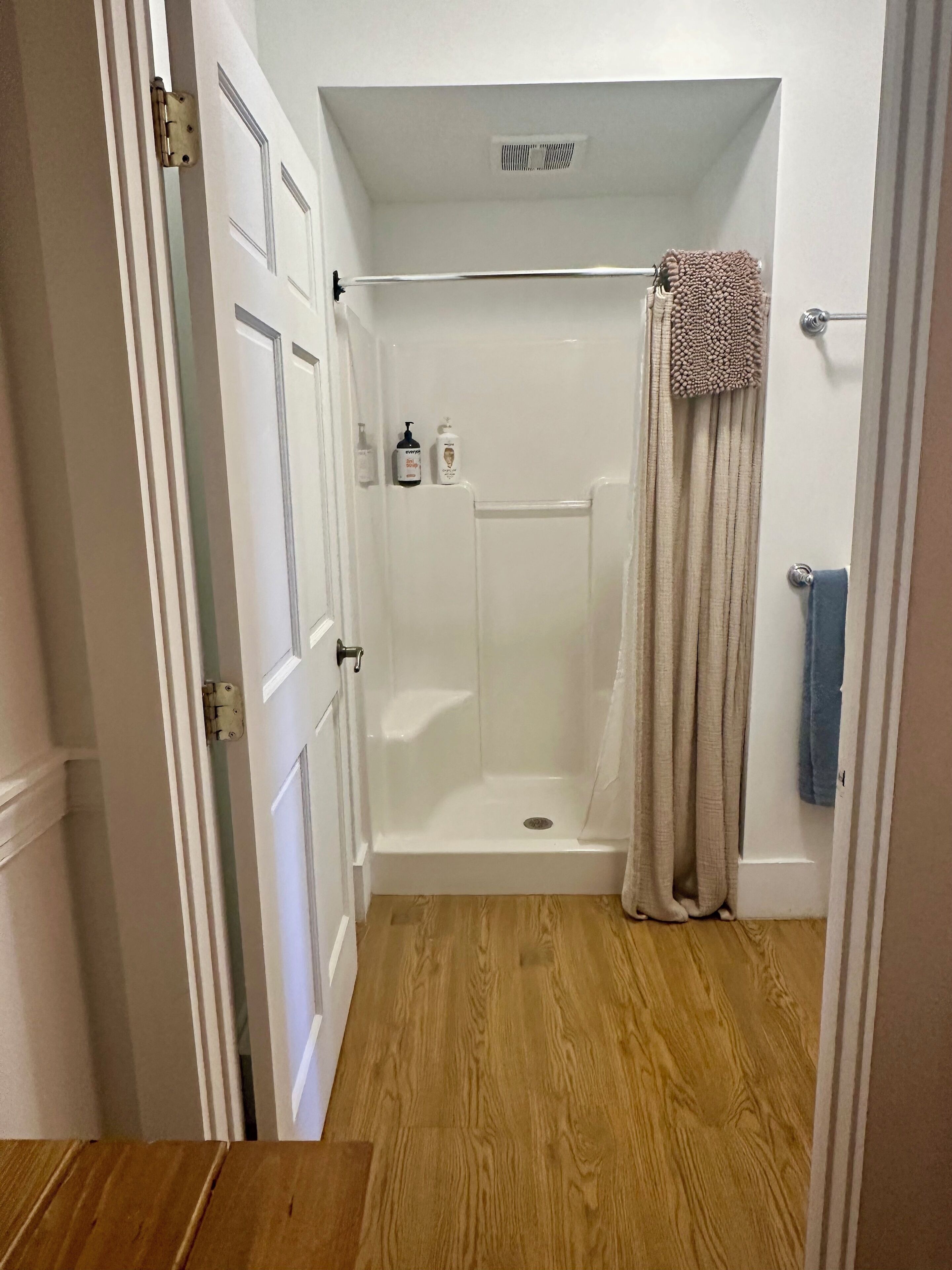 A small, enclosed shower area with a white door, a shower curtain, and a towel rack.