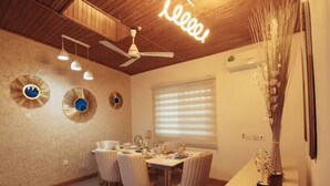 A dining area with a wooden ceiling, ceiling fan, and three pendant lights. There are round wall decorations and a window with blinds.