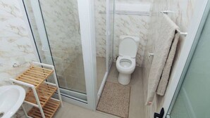 Ein Badezimmer mit Duschkabine aus Glas, Toilette, Waschbecken und Handtuchhalter.