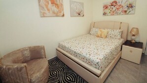 Ein Schlafzimmer mit einem Bett, einem Sessel, einem Nachttisch und zwei an der Wand befestigten Bildern.