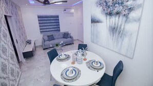 A dining area with a round table set for four, a grey sofa, and a large abstract painting on the wall. - B&B Charming bed & breakfast in gorgeous Accra with WiFi, AC (Accra)
