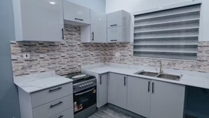 A modern kitchen with white cabinets, a built-in stove, and a large window with horizontal blinds. - B&B Charming bed & breakfast in gorgeous Accra with WiFi, AC (Accra)