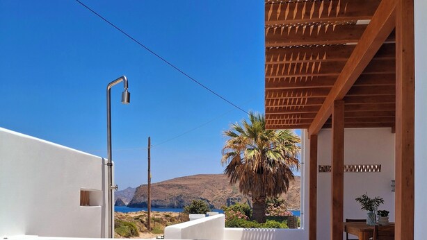 A swimming pool with clear blue water, a pergola with wooden beams, a dining area with a table and chairs, and a view of a mountainous landscape. - Famly Apartment with Sea View & Plunge Pool (Ground Floor) (Milos)