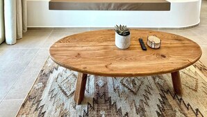A modern living room with a curved bench, a round wooden coffee table, and a patterned rug. - Famly Apartment with Sea View & Plunge Pool (Ground Floor) (Milos)