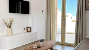 A modern living room with a flat-screen TV, a wooden coffee table, a sofa, a patterned rug, and a sliding glass door leading to an outdoor area. - Famly Apartment with Sea View & Plunge Pool (Ground Floor) (Milos)