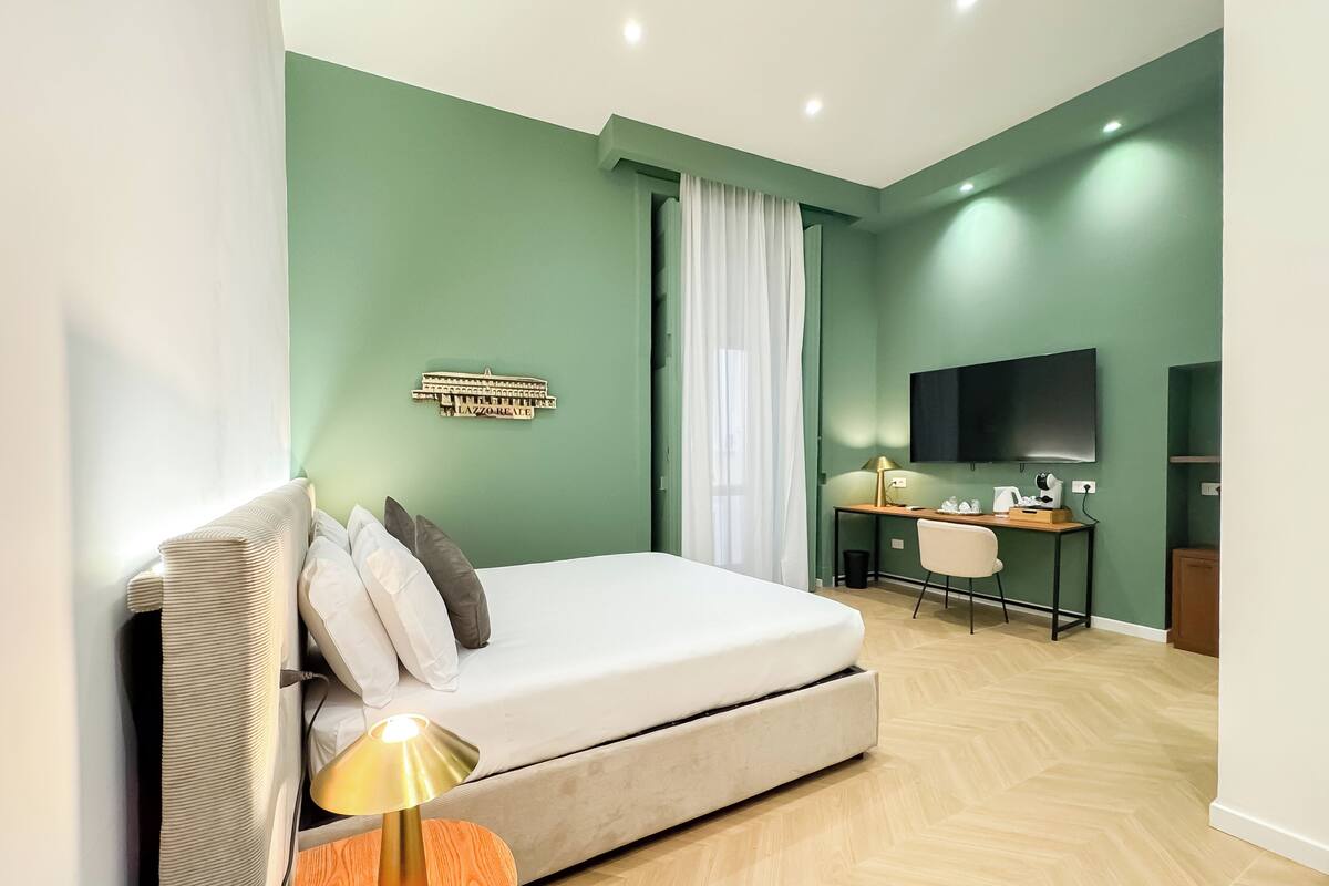 A modern hotel room with a bed, a desk, a chair, a television, and a decorative wall piece.