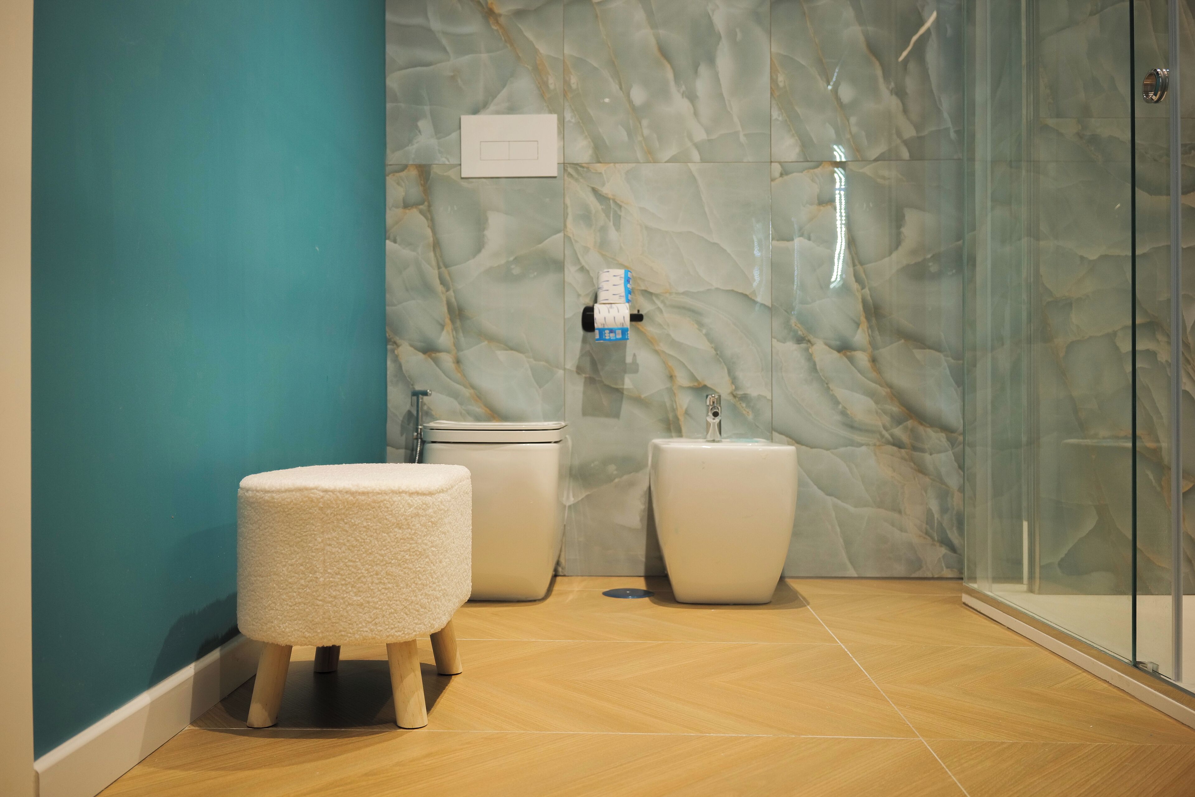Un baño moderno con pared de mármol, cabina de ducha de vidrio y un inodoro blanco.