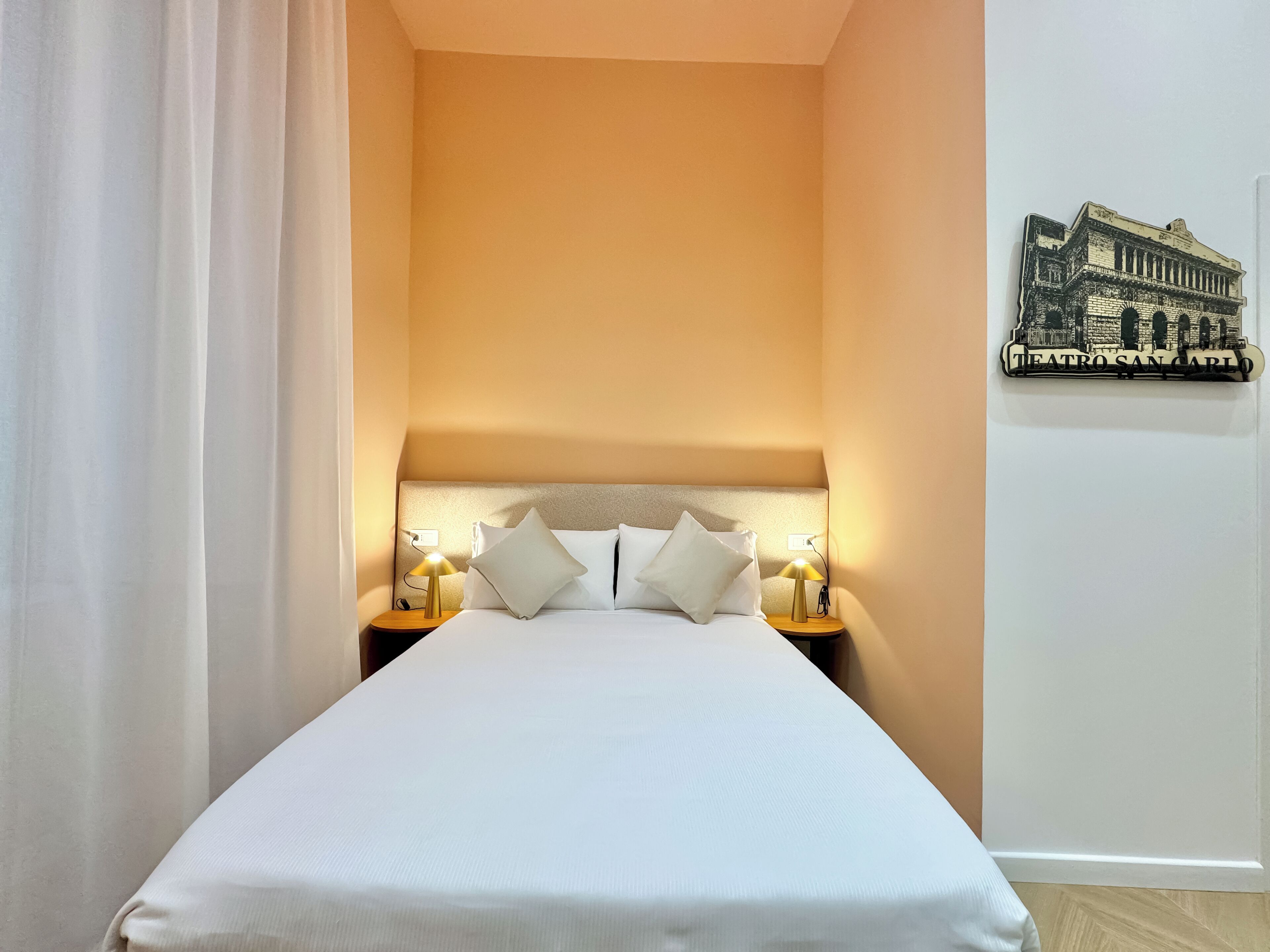 Ein Hotelzimmer mit einem Bett, zwei Nachttischen mit Lampen, einem weißen Vorhang und einer Wanddekoration.