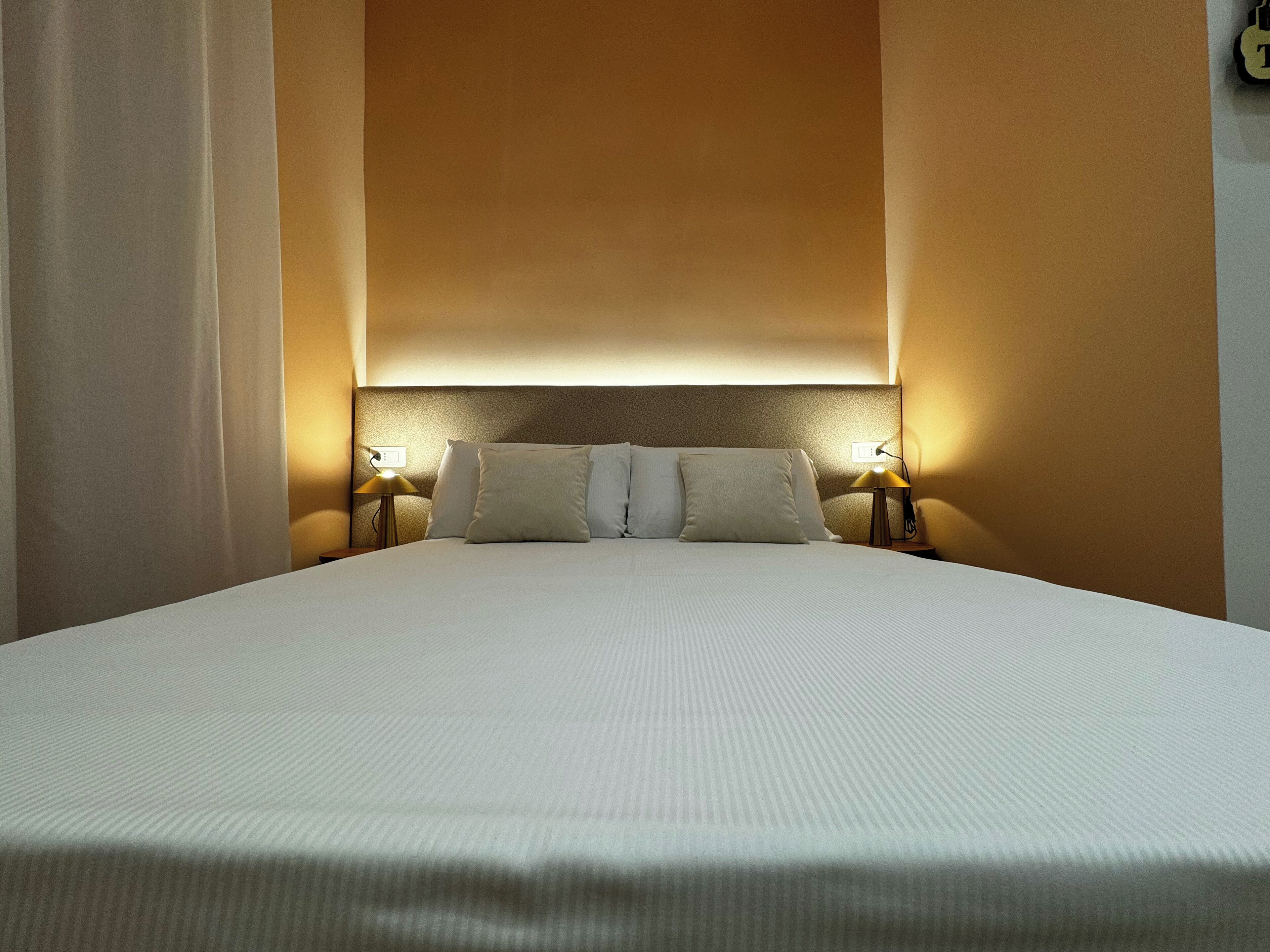 A neatly made bed with white linens, two bedside lamps, and a headboard with a textured finish.
