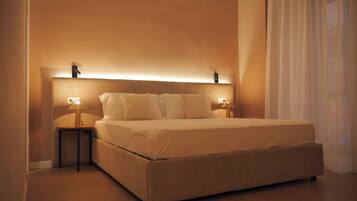 A neatly made bed with a headboard, two bedside tables with lamps, and sheer curtains.