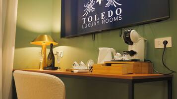 A hotel room with a desk, a lamp, a telephone, and a TV displaying "TOLEDO LUXURY ROOMS".