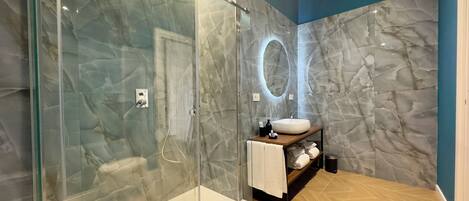 A modern bathroom with a glass-enclosed shower, a marble wall, a wooden vanity, and a round mirror.
