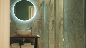 A bathroom with a round mirror, a sink, and a glass shower enclosure.
