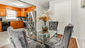 A modern kitchen with wooden cabinets, stainless steel appliances, and a glass dining table with velvet chairs.