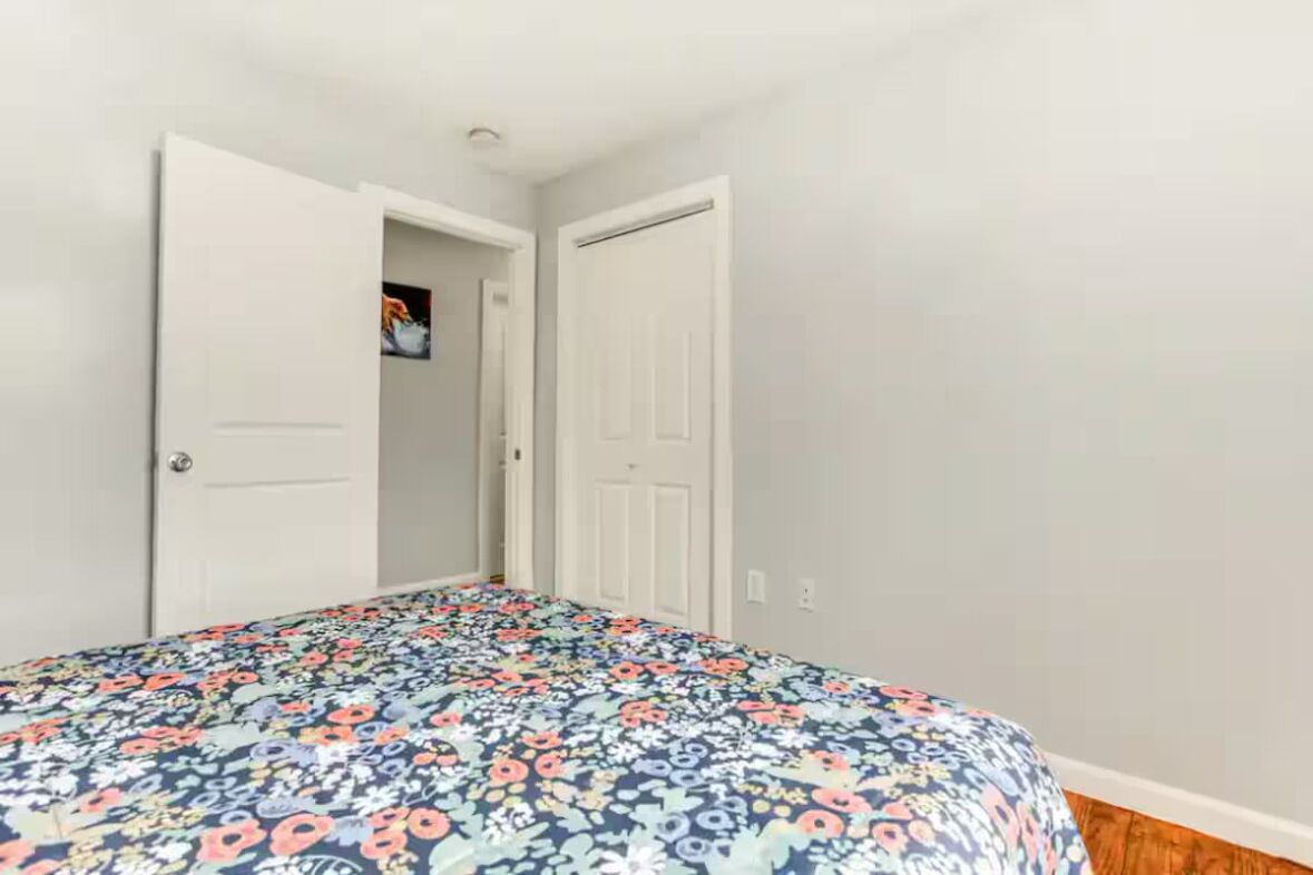 Une chambre à coucher avec une couvre-lit à motifs floraux, des murs blancs et un plancher en bois.