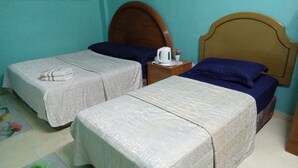 A room with two beds, a wooden headboard, a nightstand with a kettle, and a floral rug. - Al Funduq Motel 1 (Jitra)