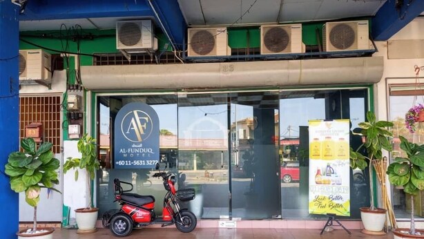 A hotel entrance with a signboard, air conditioning units, and a parked scooter. - Al Funduq Motel 1 (Jitra)