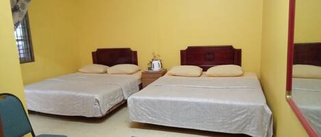A room with two beds, a small table with a kettle, and a chair.
