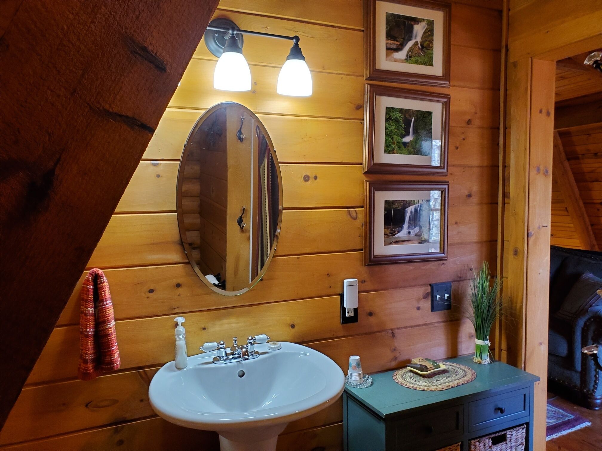 A wooden interior with a white sink, a mirror, and framed pictures on the wall.