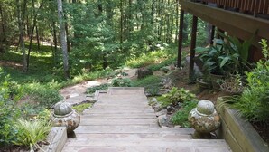 A wooden staircase leading into a forested area with stone balustrades and potted plants.