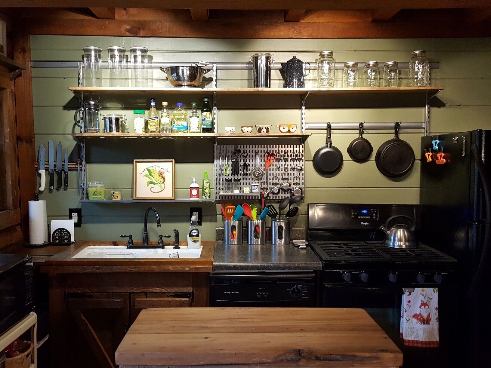 A kitchen with wooden cabinets, a sink, a stove, and various kitchen utensils and appliances.