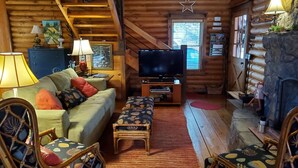 A log cabin interior with a sofa, chairs, a television, and a fireplace.