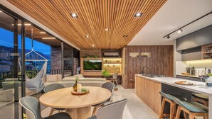Een moderne keuken met een houten plafond, een eethoek met een ronde tafel en stoelen, en een stadsgezicht door grote ramen.