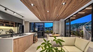 Een moderne keuken met een centraal eiland, een eetgedeelte met een ronde tafel, en een balkon met uitzicht op de stad.