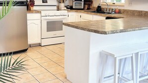 Een moderne keuken met witte kasten, een granieten aanrechtblad en een centraal eiland met barkrukken.