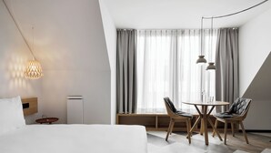 A modern hotel room with a bed, a dining area with two chairs, a table, and a ceiling light fixture. - Stay KooooK Munich City (Munich)