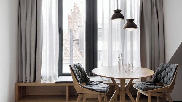 A modern dining area with a round wooden table, two cushioned chairs, and a bench. - Stay KooooK Munich City (Munich)