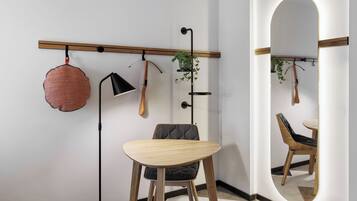 Een moderne kamer met een houten eettafel, een stoel, een hanglamp, een kamerplant aan de muur en een spiegel.