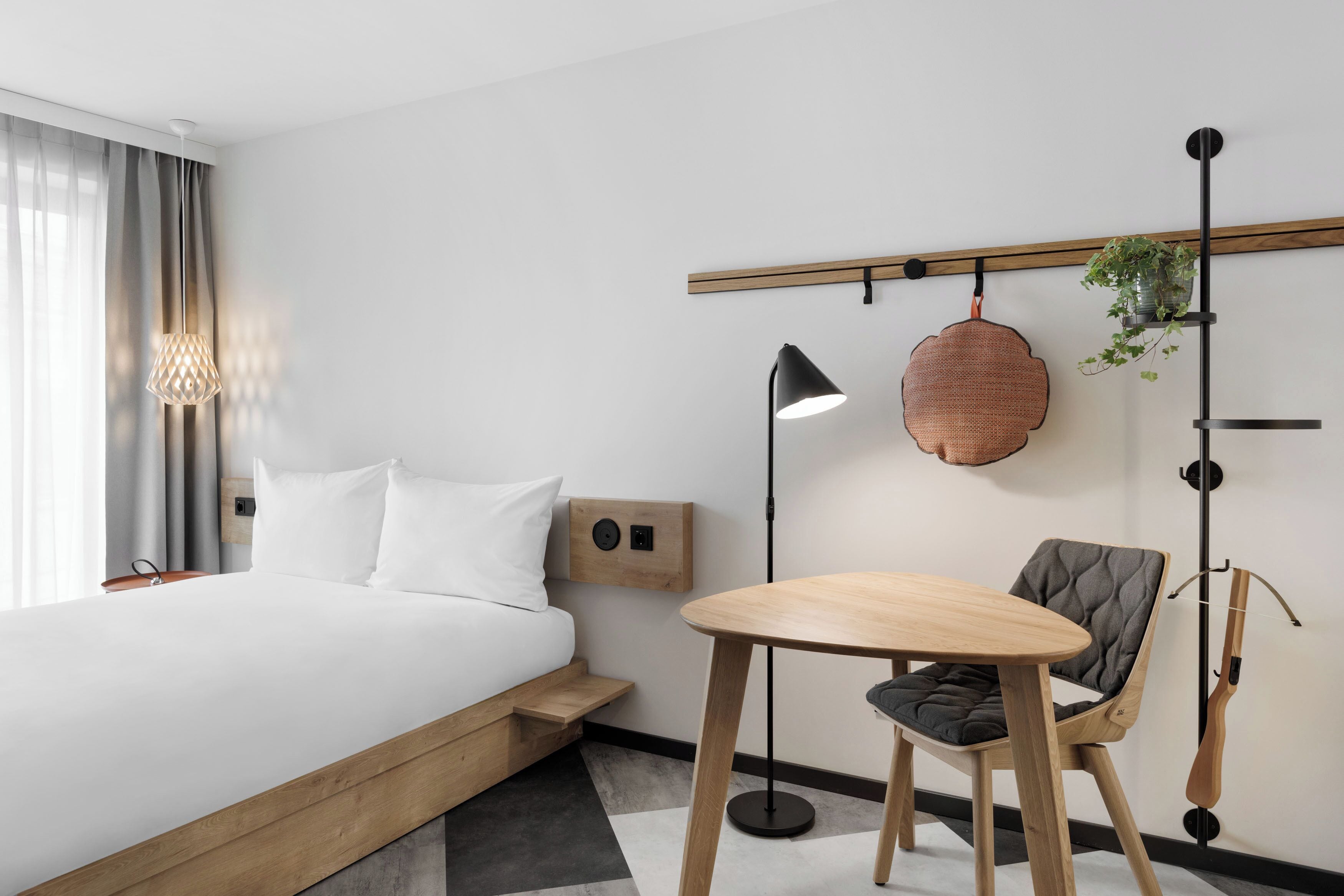 Una habitación de hotel moderna con cama, mesita de noche, lámpara, silla y una planta en maceta.