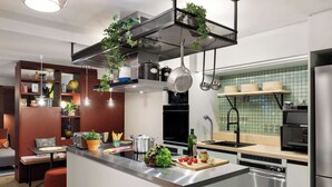 A modern kitchen with a central island, stainless steel appliances, hanging plants, and a dining area with a red bench. - Stay KooooK Munich City (Munich)