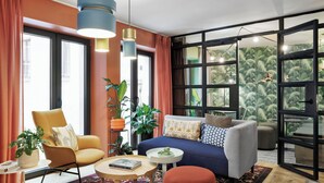 A modern living room with a sofa, armchair, and a small table. There are multiple plants and a large window with curtains. - Stay KooooK Munich City (Munich)