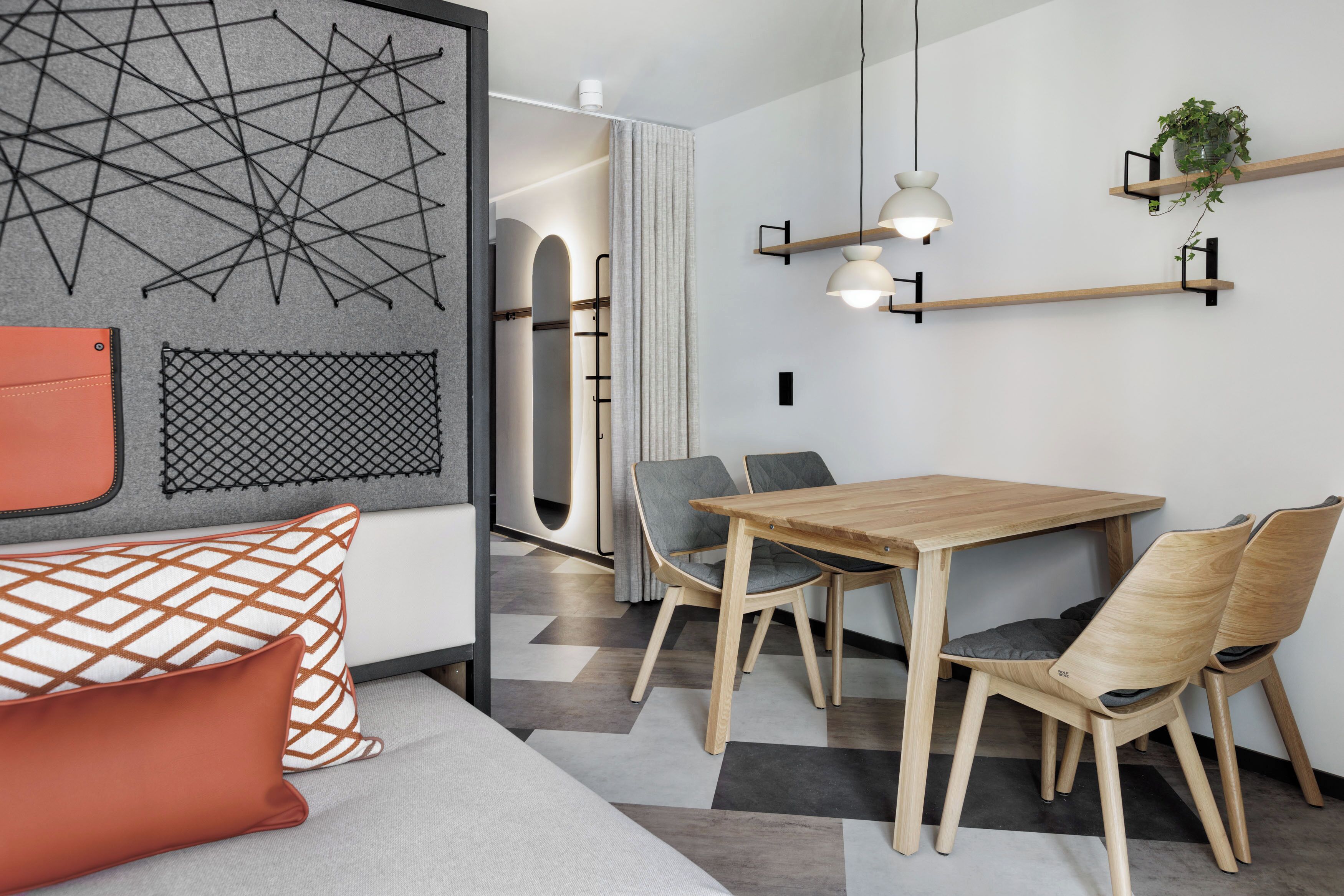 A modern interior with a wooden dining table, grey upholstered chairs, and a geometric wall art piece.