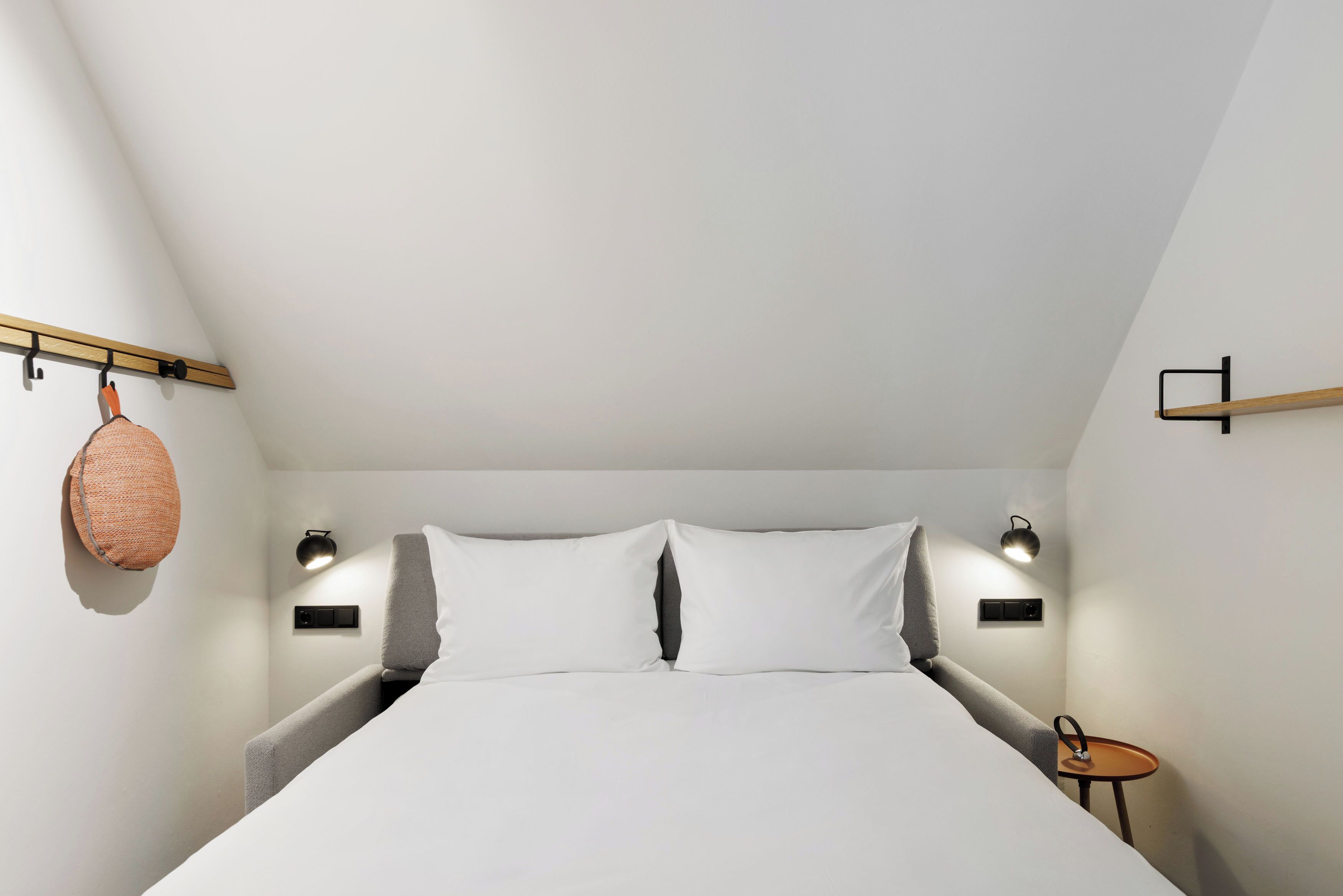 A bedroom with a bed, bedside lamps, a small table, and a hanging basket.