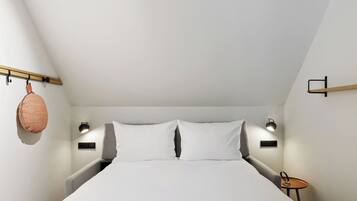 A bedroom with a bed, bedside lamps, a small table, and a hanging basket.