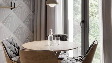 A modern dining area with a round wooden table, four upholstered chairs, a hanging pendant light, and a view through a large window.