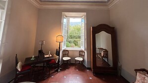 A room with a large mirror, a window with a view of greenery, a table with chairs, and a lamp.