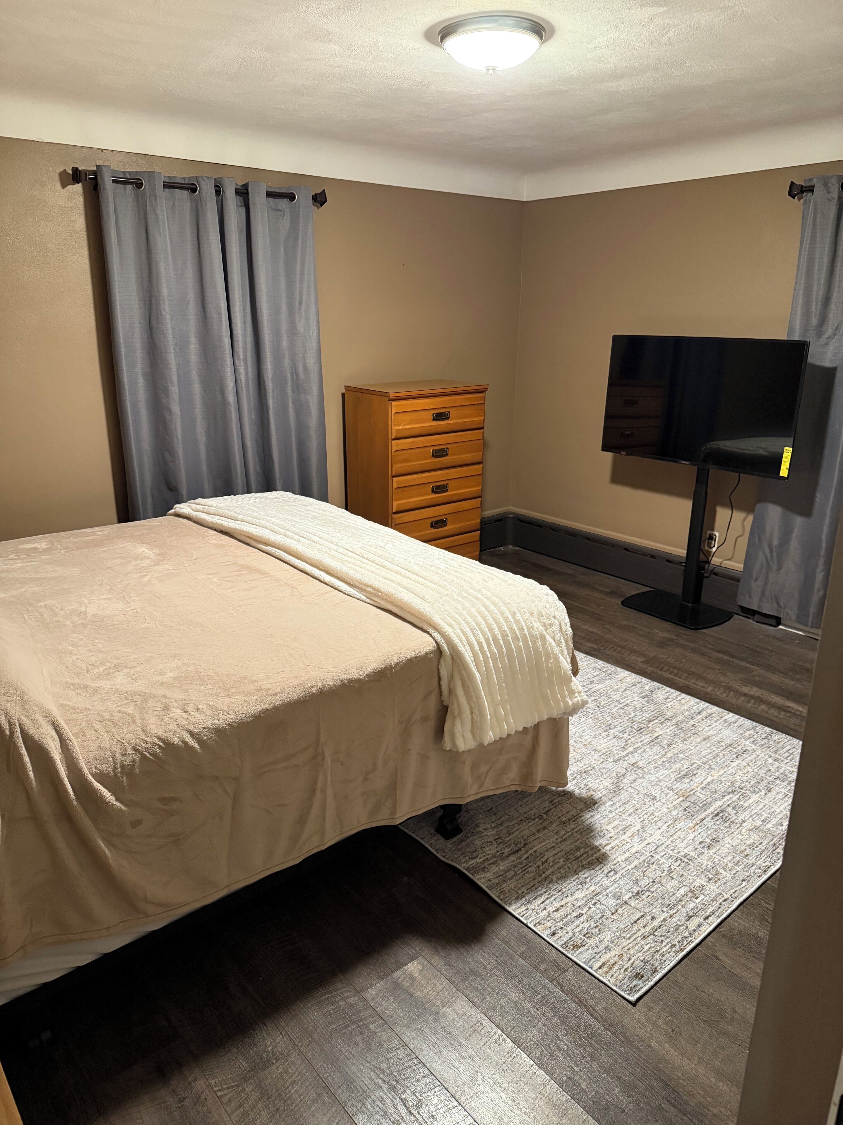 A bedroom with a bed, a dresser, a TV, and a ceiling light.