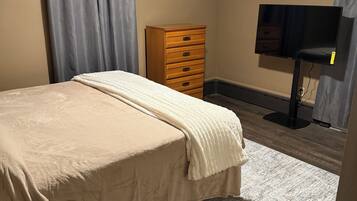 A bedroom with a bed, a dresser, a TV, and a ceiling light.
