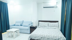 A bedroom with a bed, a nightstand, a bedside table, a lamp, a sofa, and curtains. - Charming Ocean View (Naval)
