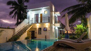 A two-story building with a swimming pool, a staircase, and a balcony with a chair. - Charming Ocean View (Naval)