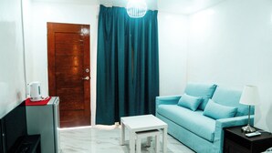 A compact living space with a teal sofa, a small white table, a coffee machine, and a lamp on a bedside table. - Charming Ocean View (Naval)