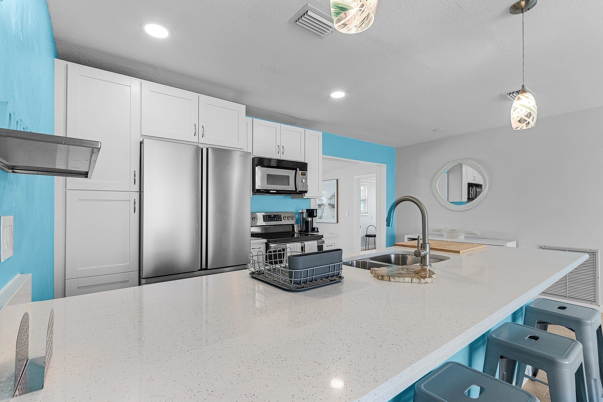 Cozinha moderna com eletrodomésticos de aço inoxidável, uma ilha grande com banquetas e uma parede azul de destaque.