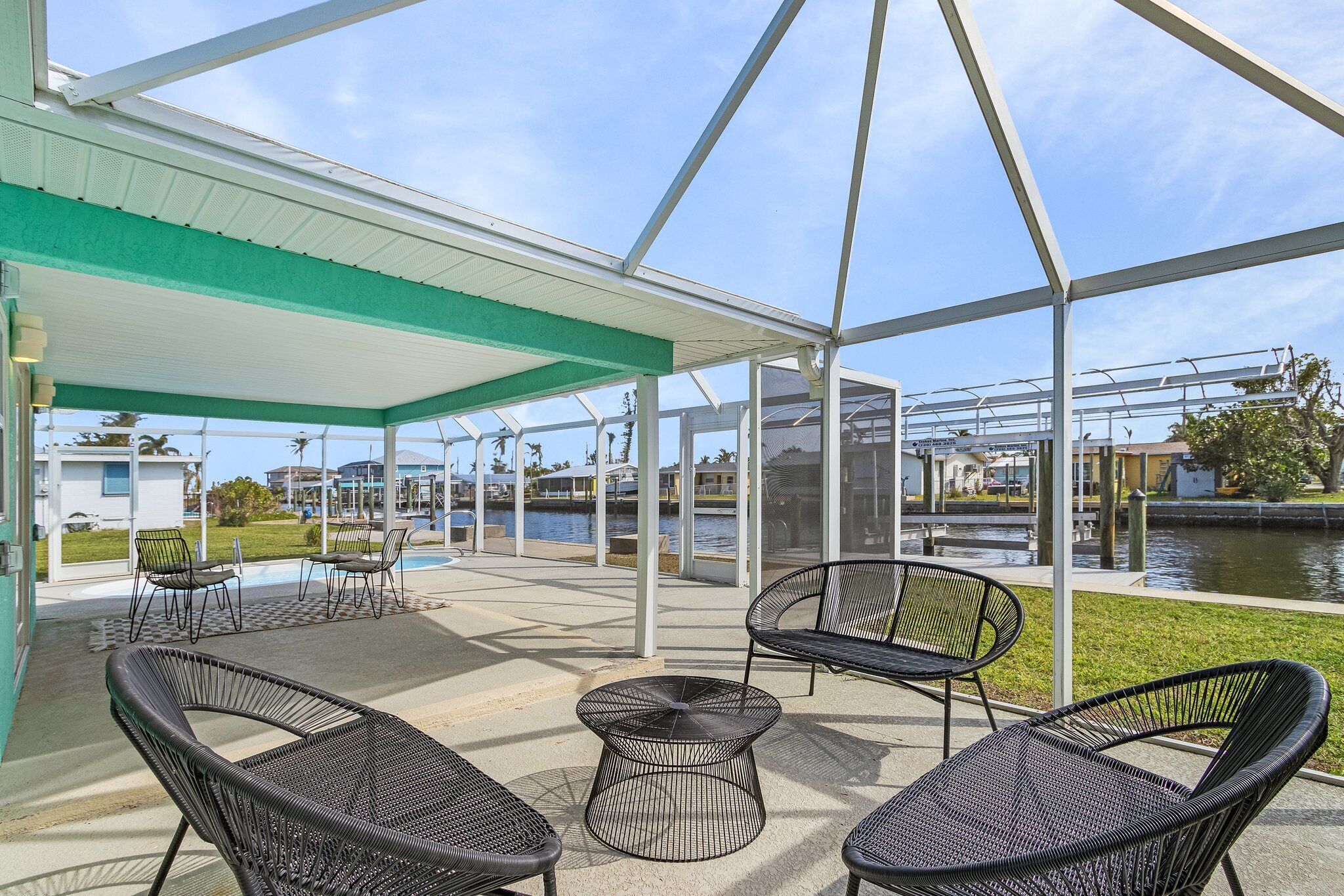 A covered outdoor area with wicker chairs and a round table, overlooking a body of water and buildings in the background.