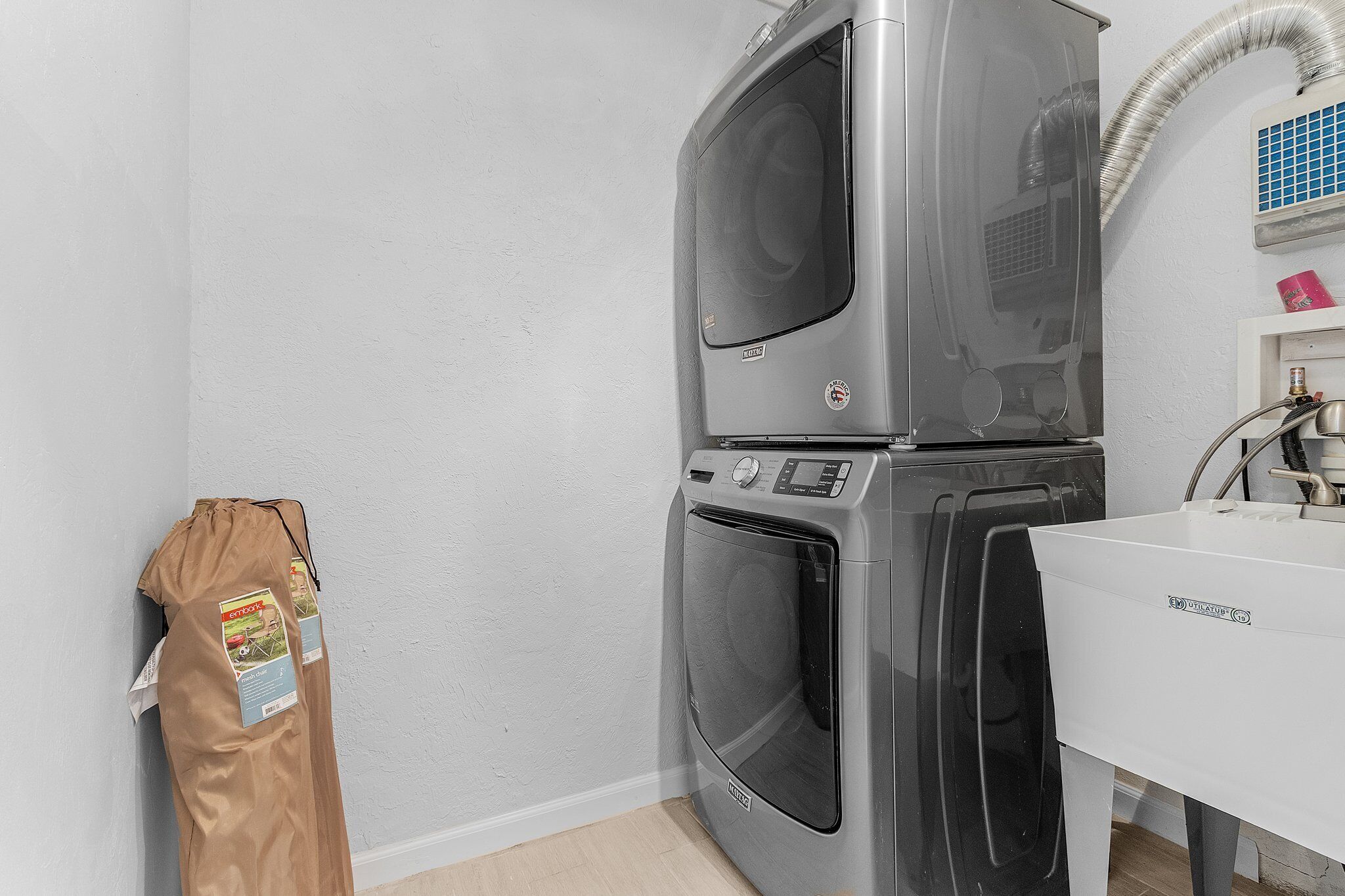 A compact laundry area with a stacked washer and dryer, a white sink, and a bag of detergent hanging on the wall.