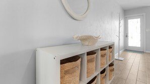 Un couloir avec une console blanche sur laquelle sont posés des paniers tressés et un bol décoratif, un miroir rond accroché au mur et une porte donnant sur une autre pièce.
