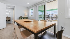 Un espace repas moderne avec une table et des chaises en bois, un petit meuble et une vue sur l’extérieur grâce à de grandes fenêtres.